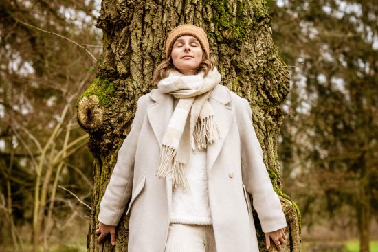 Eine hell gekleidete Frau lehnt an einer alten Eiche im herbstlichen Bad Salzufler Landschaftsgarten. Sie hat die Augen geschlossen und wirkt entspannt.