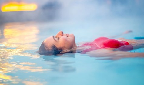 Frau liegt schwebend auf der Wasseroberfläche in einem Außenbecken der Vitasol-Therme