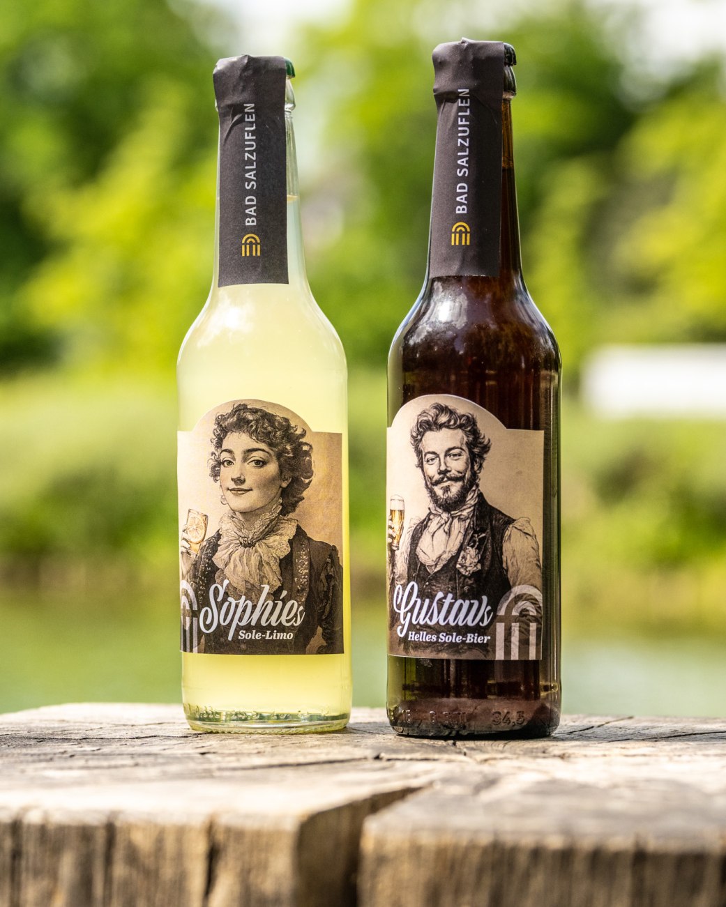 2 Getränkeflaschen stehen auf einem Holzsteg im Kurpark: Eine 0,33l Flasche Gustavs Helles Sole-Bier und eine Flasche Sophies Sole-Limo