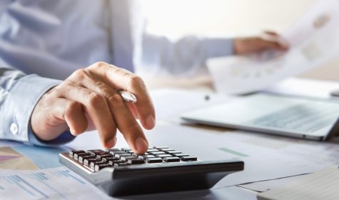 Eine Hand tippt auf einem Taschenrechner auf einem Schreibtisch, &copy; stock.adobe.com | lovelyday12