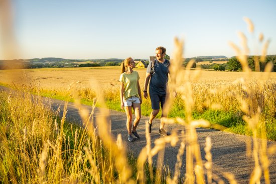 2 Personen wandern im Abendlicht im Hochsommer durch die Felder am Waldrand von Wüsten