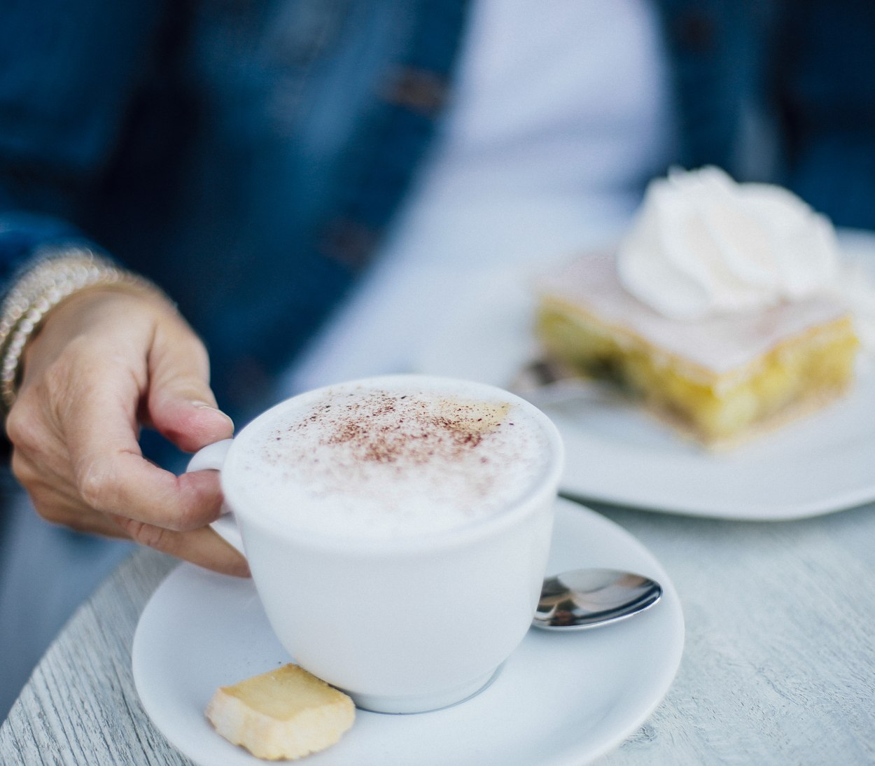 Cappuccino, Kuchen mit Sahne, auf Tisch, Hand im Hintergrund, © Staatsbad Salzuflen GmbH / S. Strothbäumer