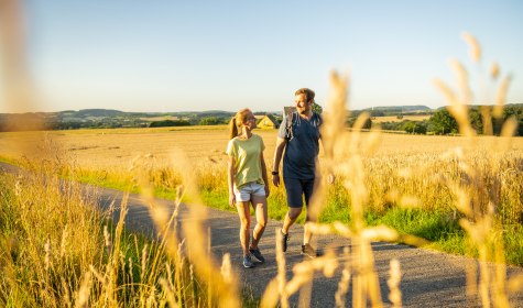2 Personen wandern im Abendlicht im Hochsommer durch die Felder am Waldrand von Wüsten