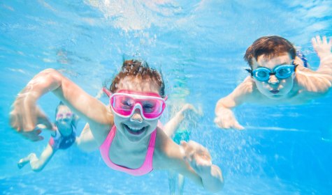 Zu sehen sind zwei Kinder mit Taucherbrillen unter Wasser in einem Schwimmbecken die lachen., © yanlev - stock.adobe.com