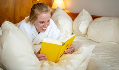 Gem&uuml;tlich entspannende und lesende Frau im Bademantel auf ihrem Zimmer 